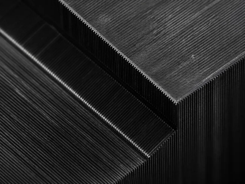 Macro view of a precision-milled dark metal block, dense parallel grooves running to a sharp square corner.